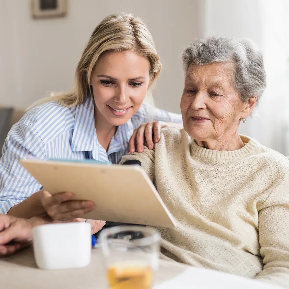 Pflegerin schaut mit einer Seniorin Unterlagen auf dem Tablet an