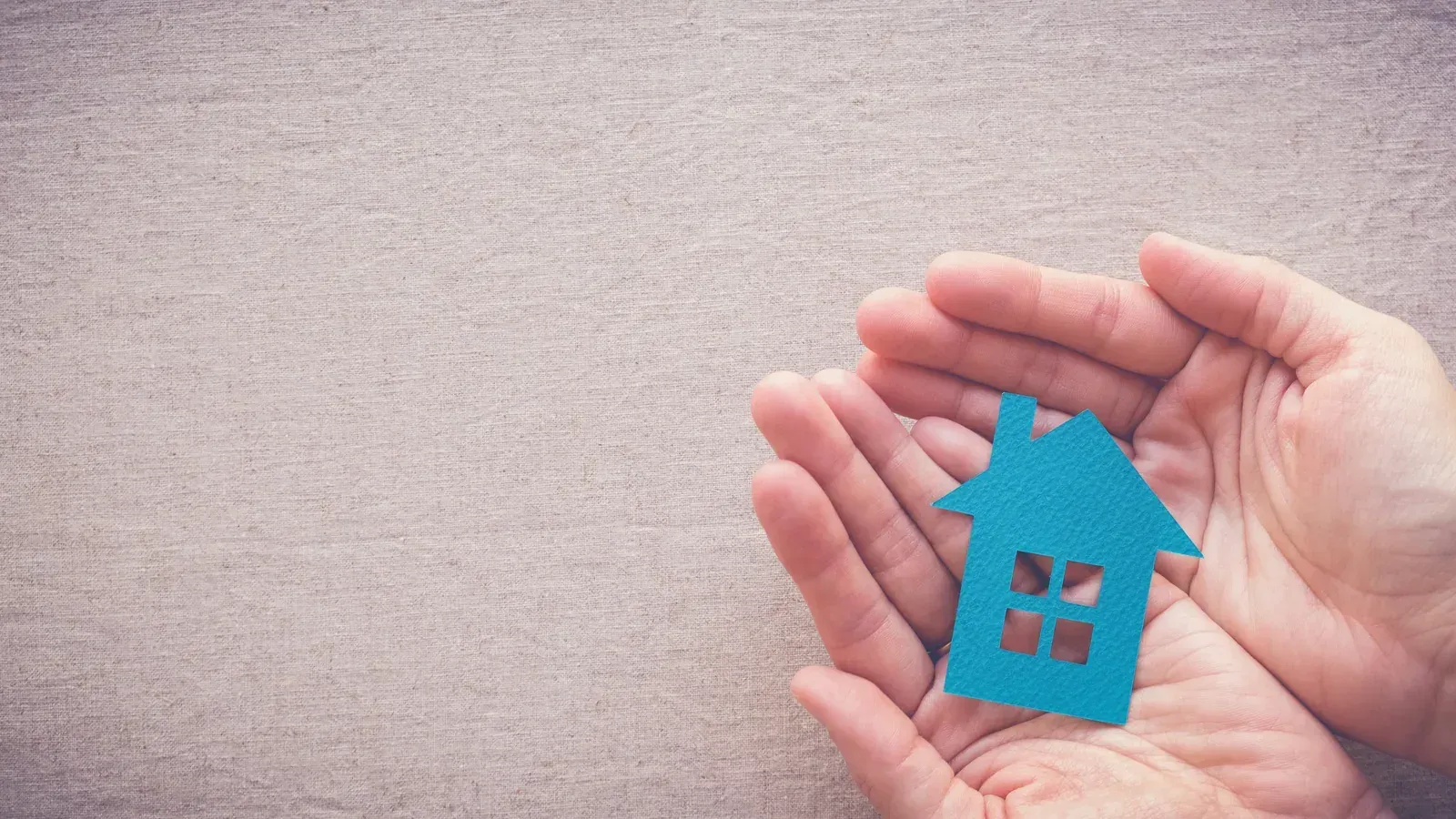 Hände halten ein blaues Haus – Sicherheit und Geborgenheit zu Hause